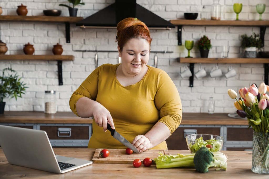 overweight running beginner cutting vegetables to prepare healthy food