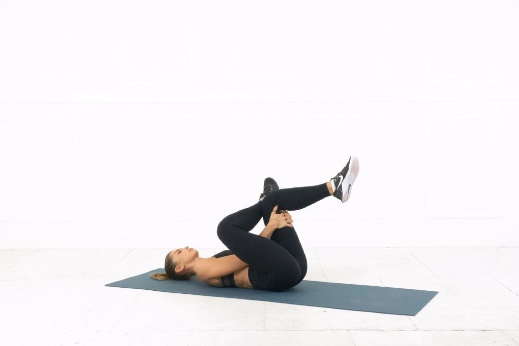 runner lying down on a yoga mat doing a glute stretch